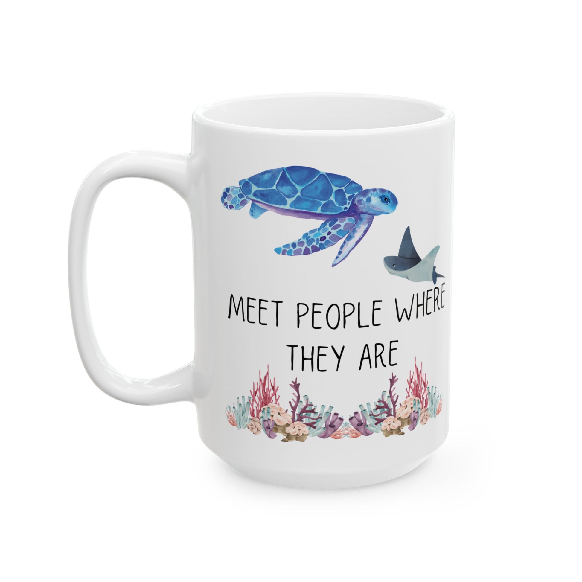 White ceramic coffee mug with a sea turtle swimming above a sting ray and the phrase "meet people where they are" and coral lining the bottom